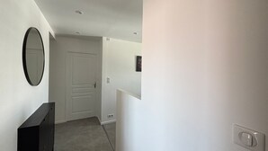 A hallway with a white door, a black dresser, and a wall-mounted mirror. - Renovated 2BR Apartment, Sleeps 5, City Center, Close to Beach, Parking, WiFi (Les Sables-d'Olonne)