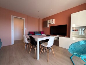 A modern kitchen with a dining area, white cabinetry, a flat-screen TV, and a teal chair. - Renovated 2BR Apartment, Sleeps 5, City Center, Close to Beach, Parking, WiFi (Les Sables-d'Olonne)