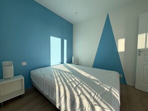 A bedroom with a bed, a nightstand, a lamp, and a window. - Renovated 2BR Apartment, Sleeps 5, City Center, Close to Beach, Parking, WiFi (Les Sables-d'Olonne)