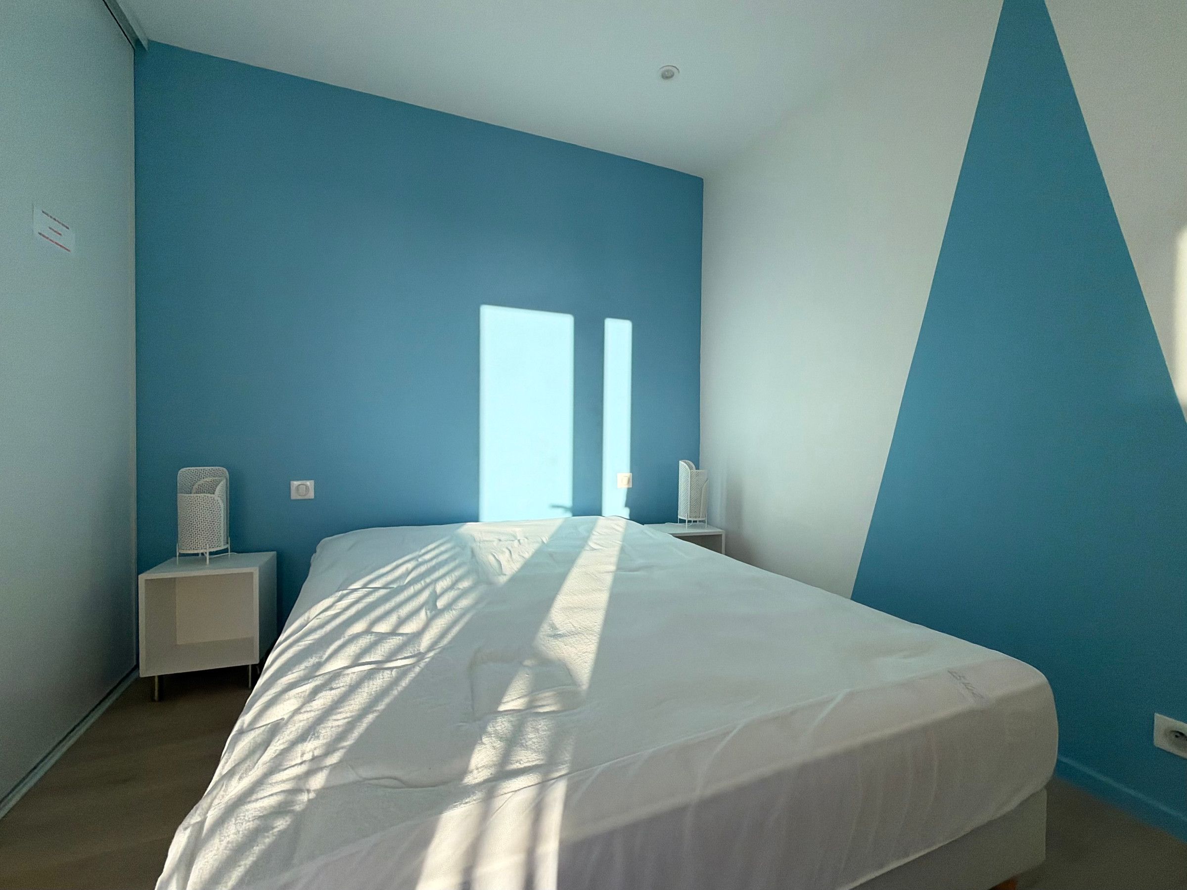 Ein Schlafzimmer mit einem Bett, zwei Nachttischen und einem Fenster mit Jalousien.