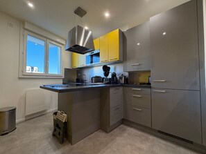 Een moderne keuken met grijze kastjes, een roestvrijstalen afzuigkap en een raam dat voor natuurlijk licht zorgt.