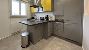A modern kitchen with grey cabinets, a stainless steel range hood, and a window providing natural light. - Renovated 2BR Apartment, Sleeps 5, City Center, Close to Beach, Parking, WiFi (Les Sables-d'Olonne)