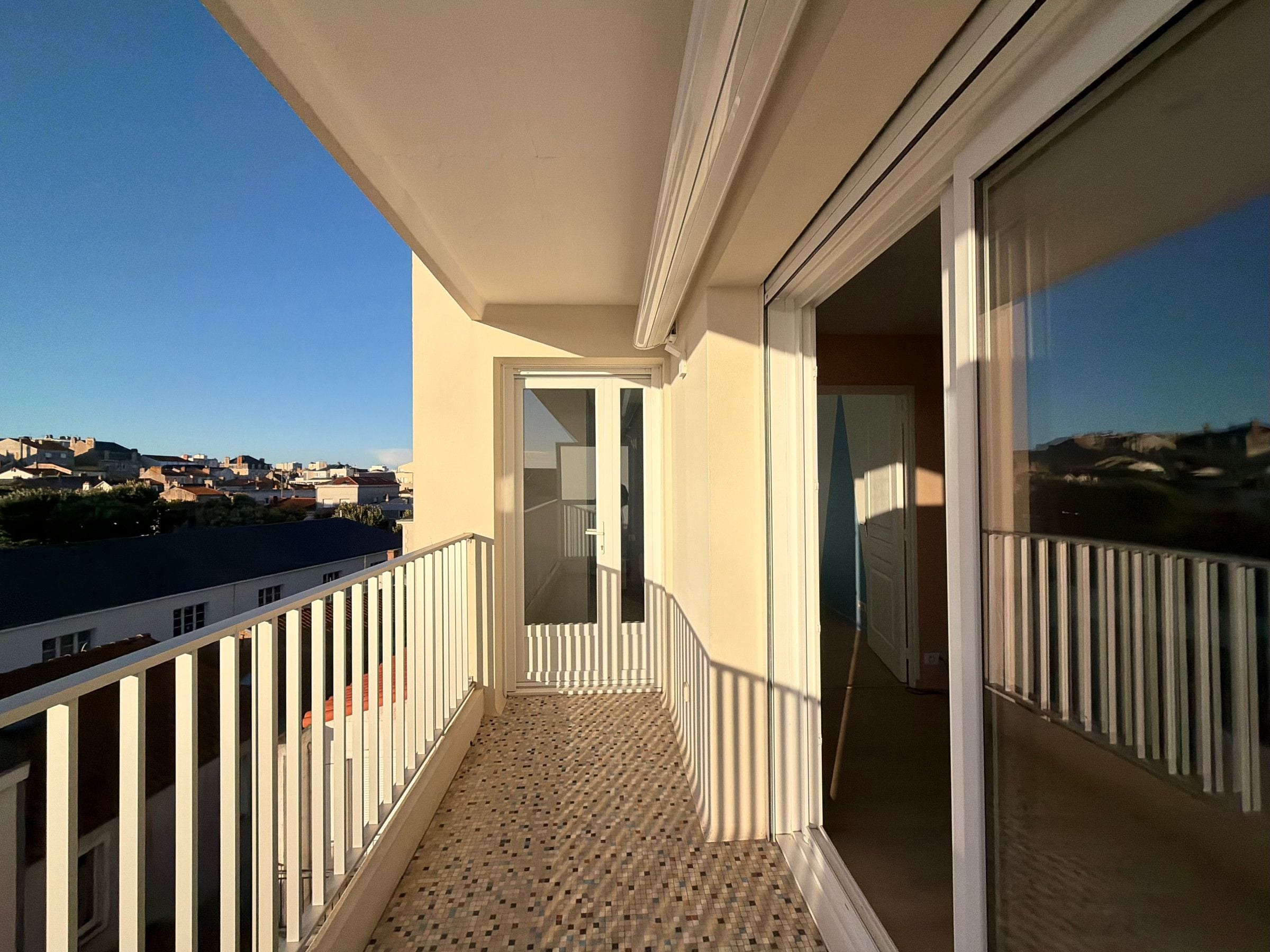 Un balcon doté d’un sol carrelé, d’une balustrade blanche et offrant une vue sur la ville.