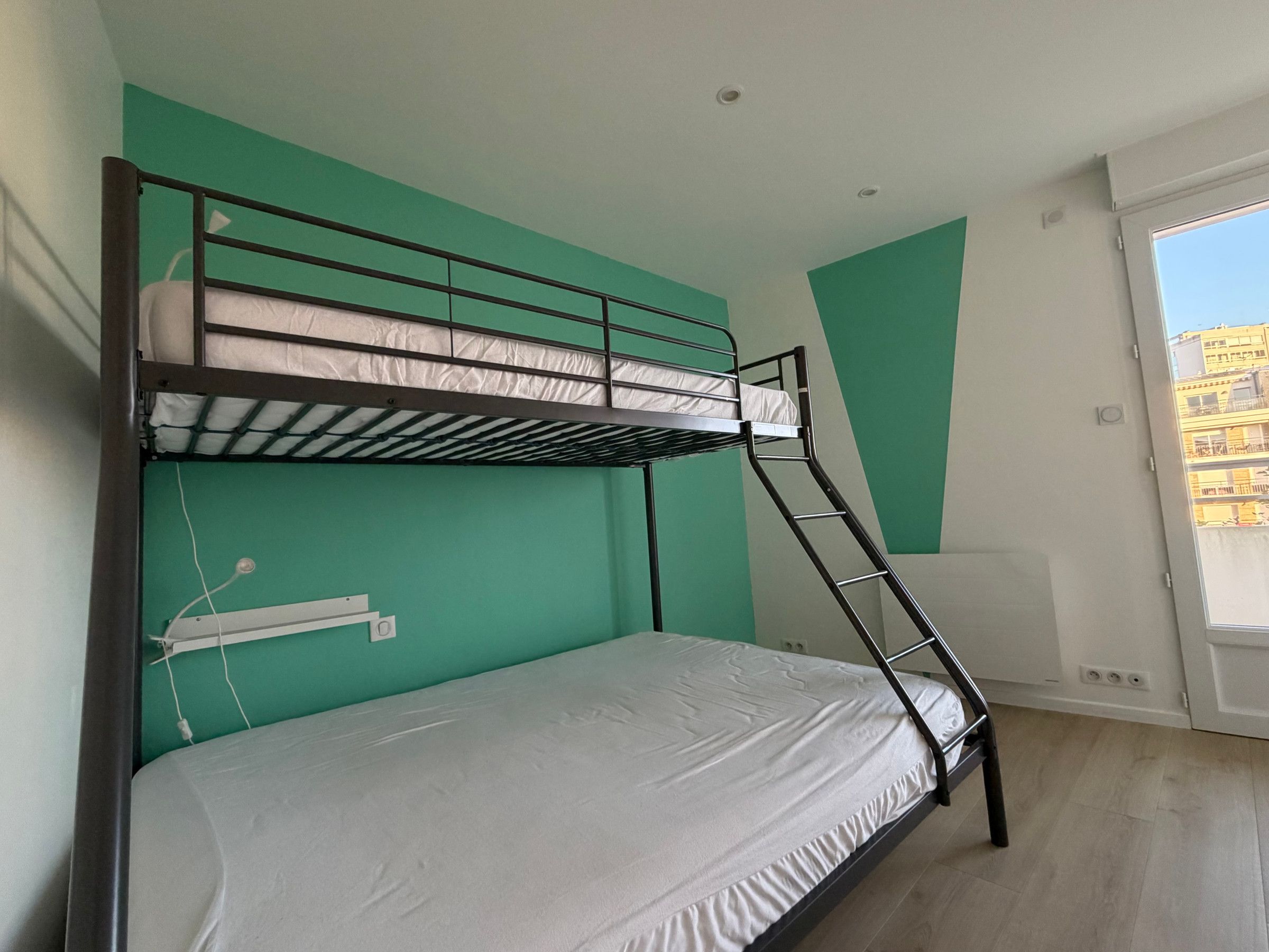 Ein Stockbett in einem Zimmer mit türkisfarbenen Wänden und einem Fenster.