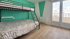 A room with a bunk bed, a window with a view of buildings, and a white radiator. - Renovated 2BR Apartment, Sleeps 5, City Center, Close to Beach, Parking, WiFi (Les Sables-d'Olonne)