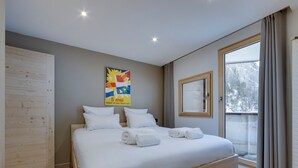 A modern hotel room with a large bed, a wooden wardrobe, a window with curtains, and a poster on the wall. - Renovated apartment at the slopes, pets allowed (Val-d'Isère)