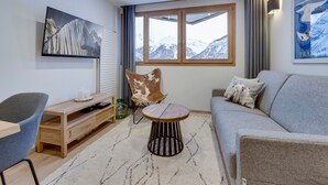 A modern living room with a sofa, a chair, a small round table, and a TV mounted on the wall. - Renovated apartment at the slopes, pets allowed (Val-d'Isère)