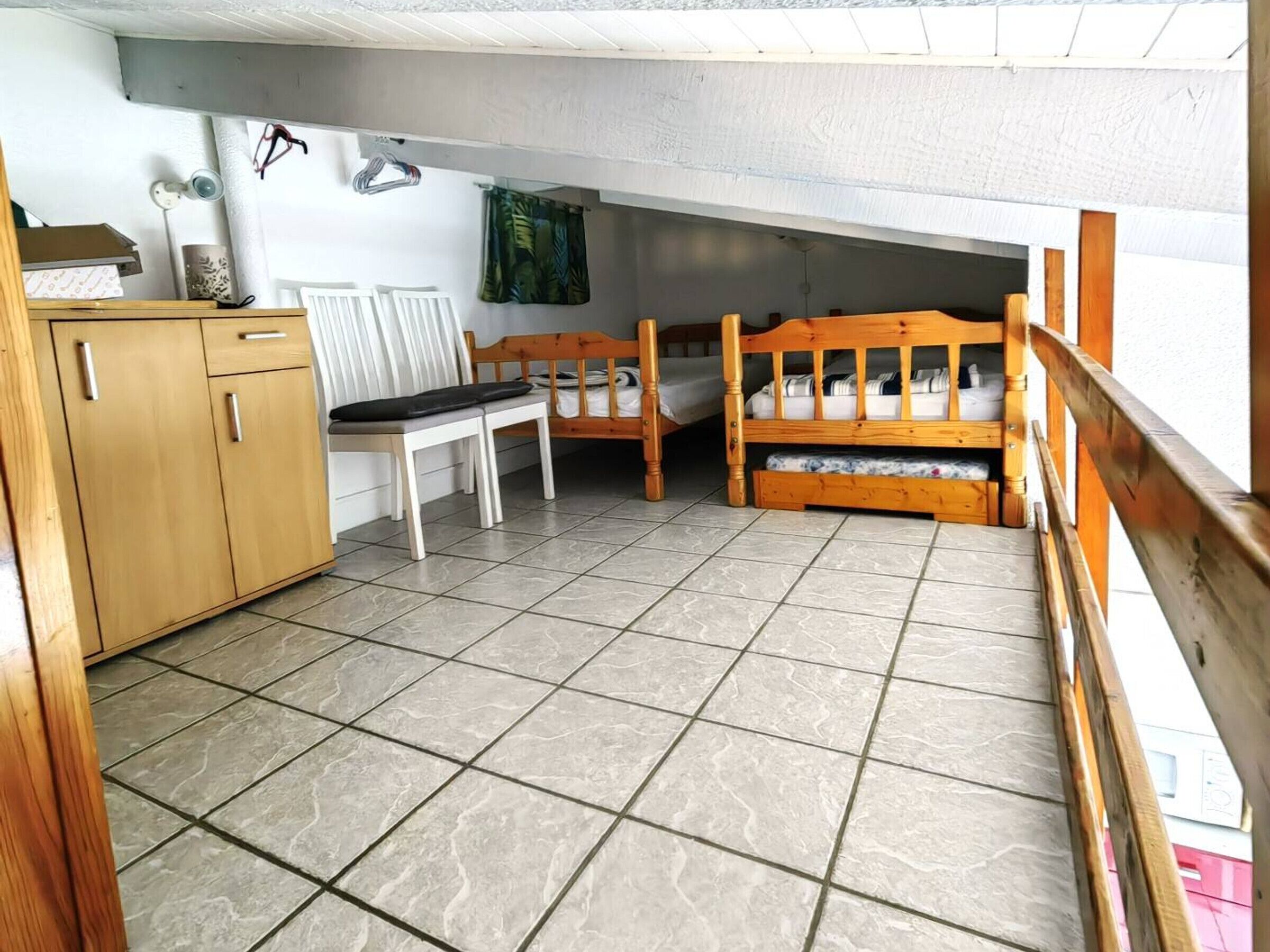 Ein Schlafsaalzimmer mit zwei Holzbettgestellen, einem Holzschrank, einem weißen Stuhl und einem Fliesenboden.