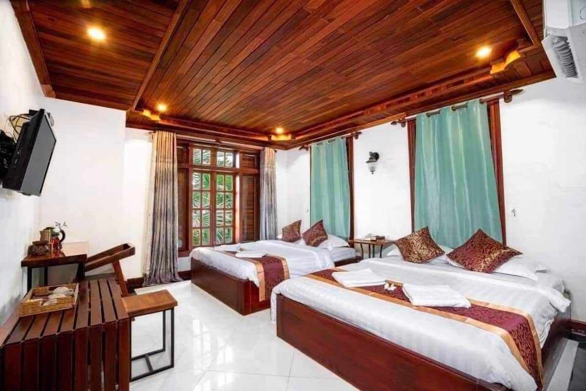 A hotel room with two beds, wooden ceiling, a TV, and a desk with a chair.