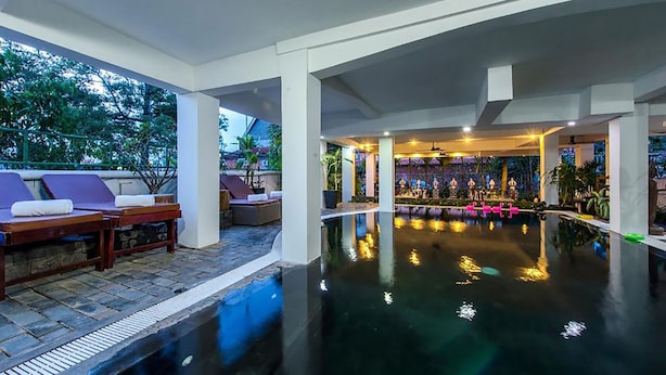 Zona de piscina con sillas de descanso y un bar con asientos y plantas.