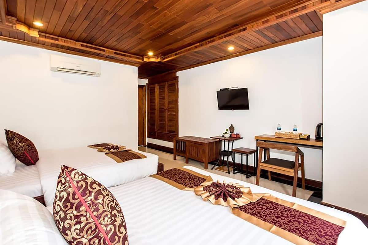A hotel room with two beds, a desk, a TV, and a wooden ceiling.