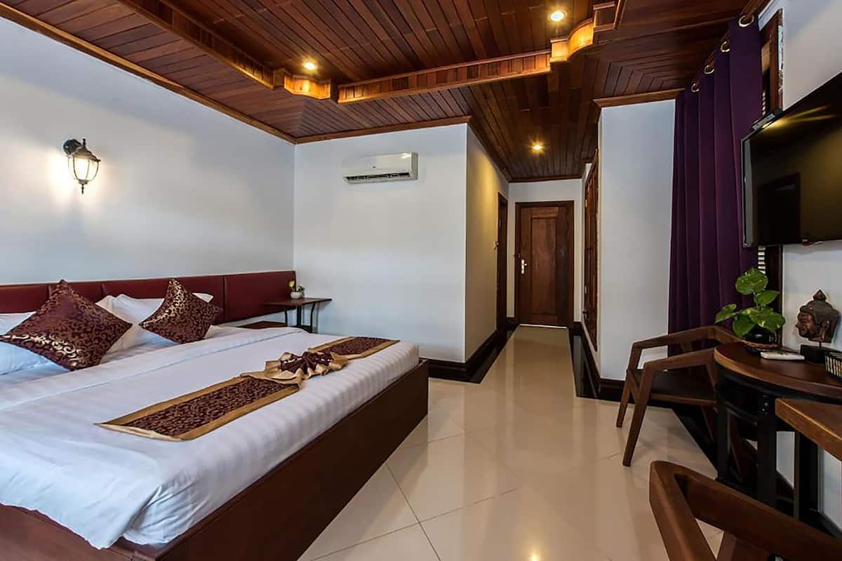 A hotel room with a bed, bedside table, lamp, air conditioning unit, and a TV.