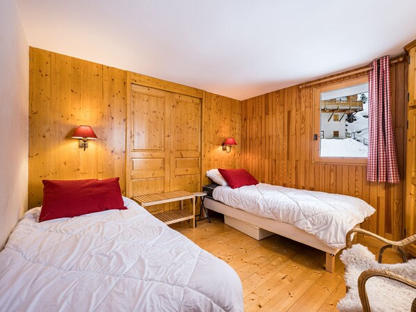 A room with two beds, wooden walls, and a window with a view of a snowy landscape.