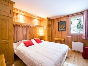 A wooden-paneled room with a bed, a window with a view of a snowy landscape, and a framed picture on the wall.