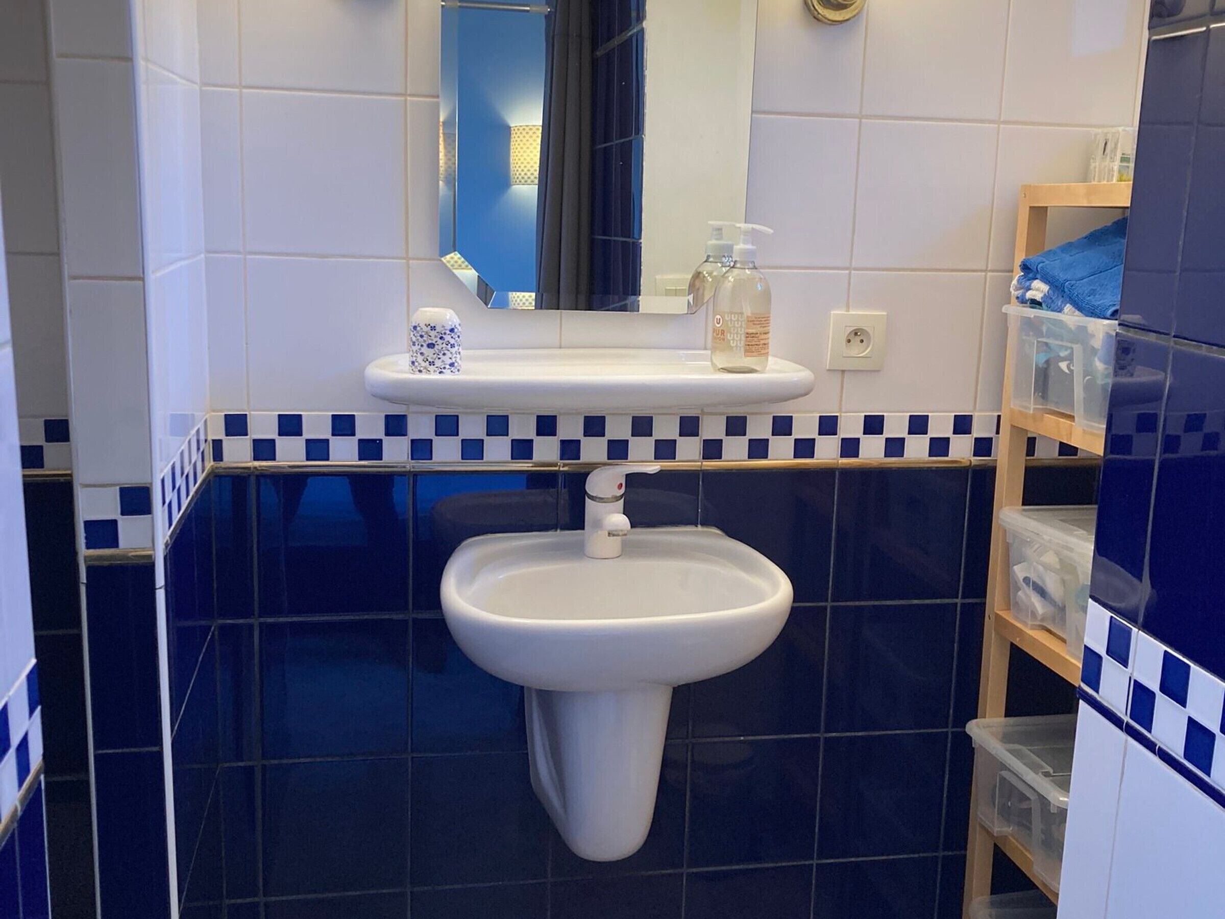 Une salle de bain avec un lavabo blanc, un miroir et un sol carrelé de carreaux bleus.