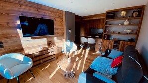 A modern living room with a flat-screen TV, wooden flooring, a sofa, and a dining area.