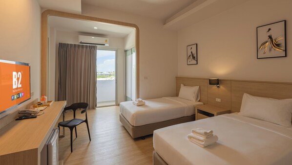 A hotel room with two beds, a desk with a chair, a TV, and artwork on the walls.