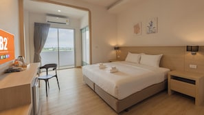 A hotel room with a bed, bedside table, chair, and a desk with a computer and a coffee maker.