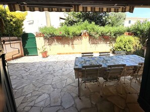 Um pátio externo com piso de pedra, uma mesa com cadeiras e plantas em vasos.