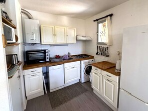 Cozinha compacta com armários brancos, micro-ondas, torradeira, fogão, máquina de lavar e geladeira.
