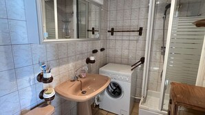 A compact bathroom with a sink, toilet, and washing machine, featuring tiled walls and a wooden ceiling. - 2-Room Pavilion with Parking, Near Beach, 6 People (Valras-Plage)