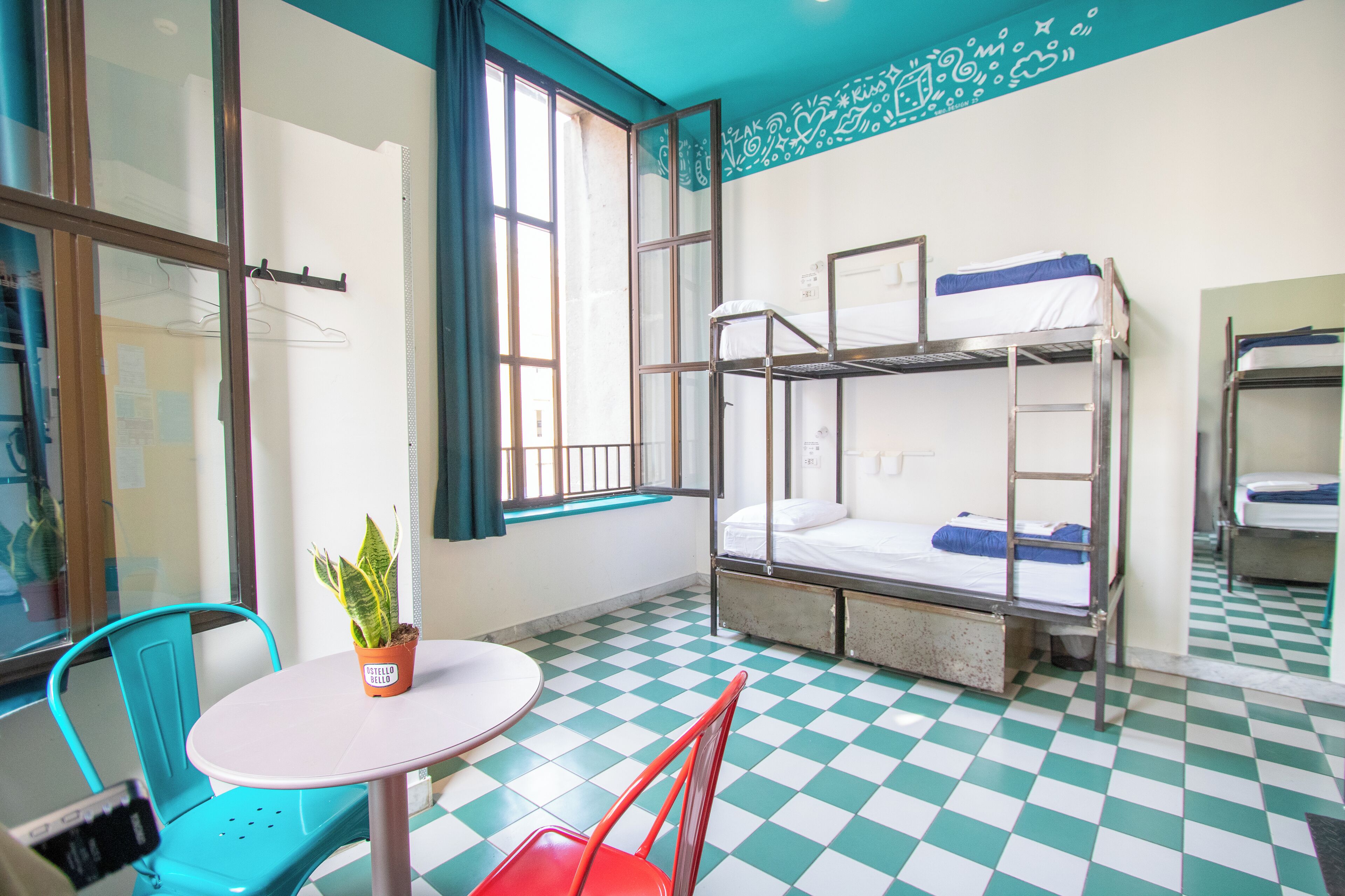 Une chambre de dortoir avec des lits superposés, une table ronde, des chaises et une plante en pot.