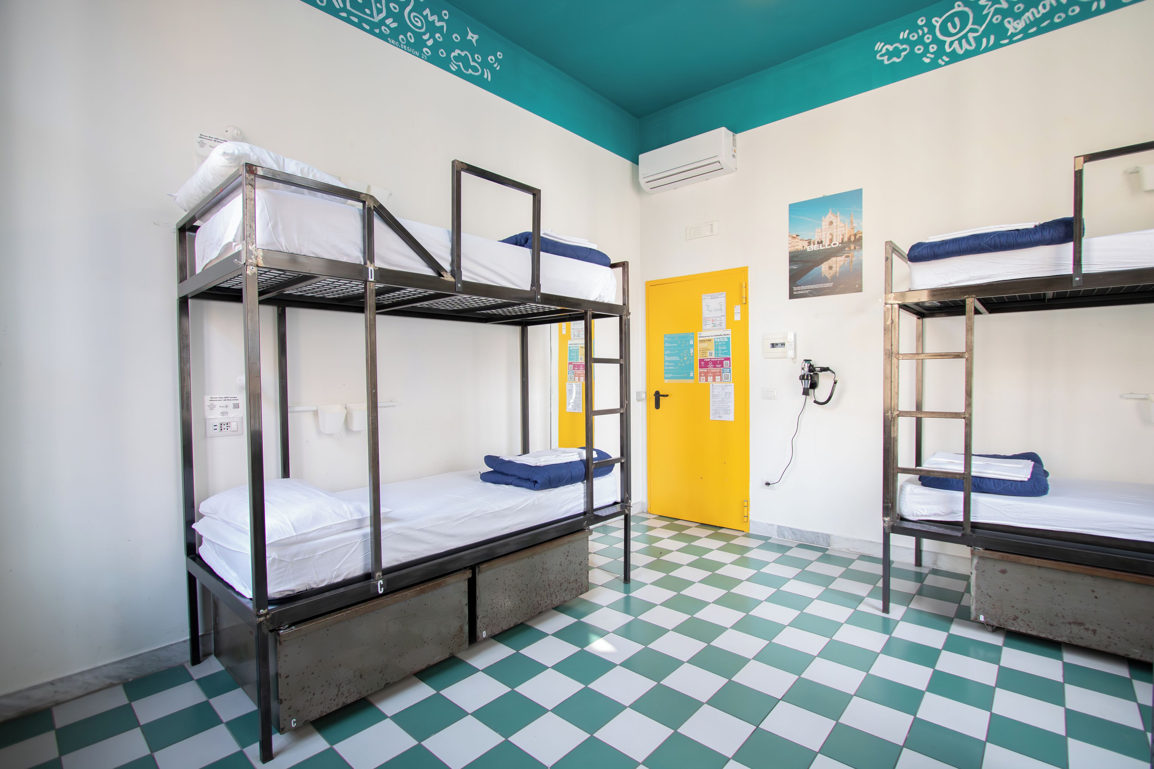 Ein Schlafsaalzimmer mit Etagenbetten, einem Schachbrettfußboden, einer gelben Tür und einer Wandklimaanlage.