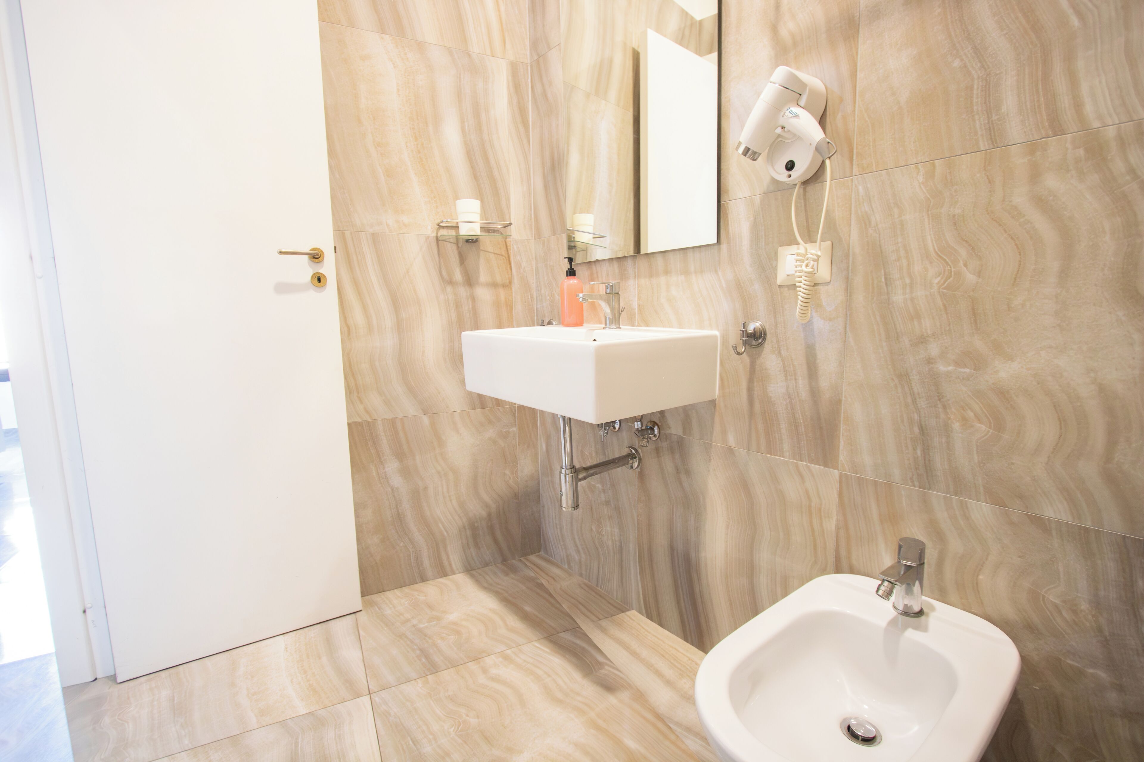 Ein modernes Badezimmer mit Waschbecken, Bidet und Spiegel. Eine Handtuchstange und ein Fön sind an der Wand angebracht.