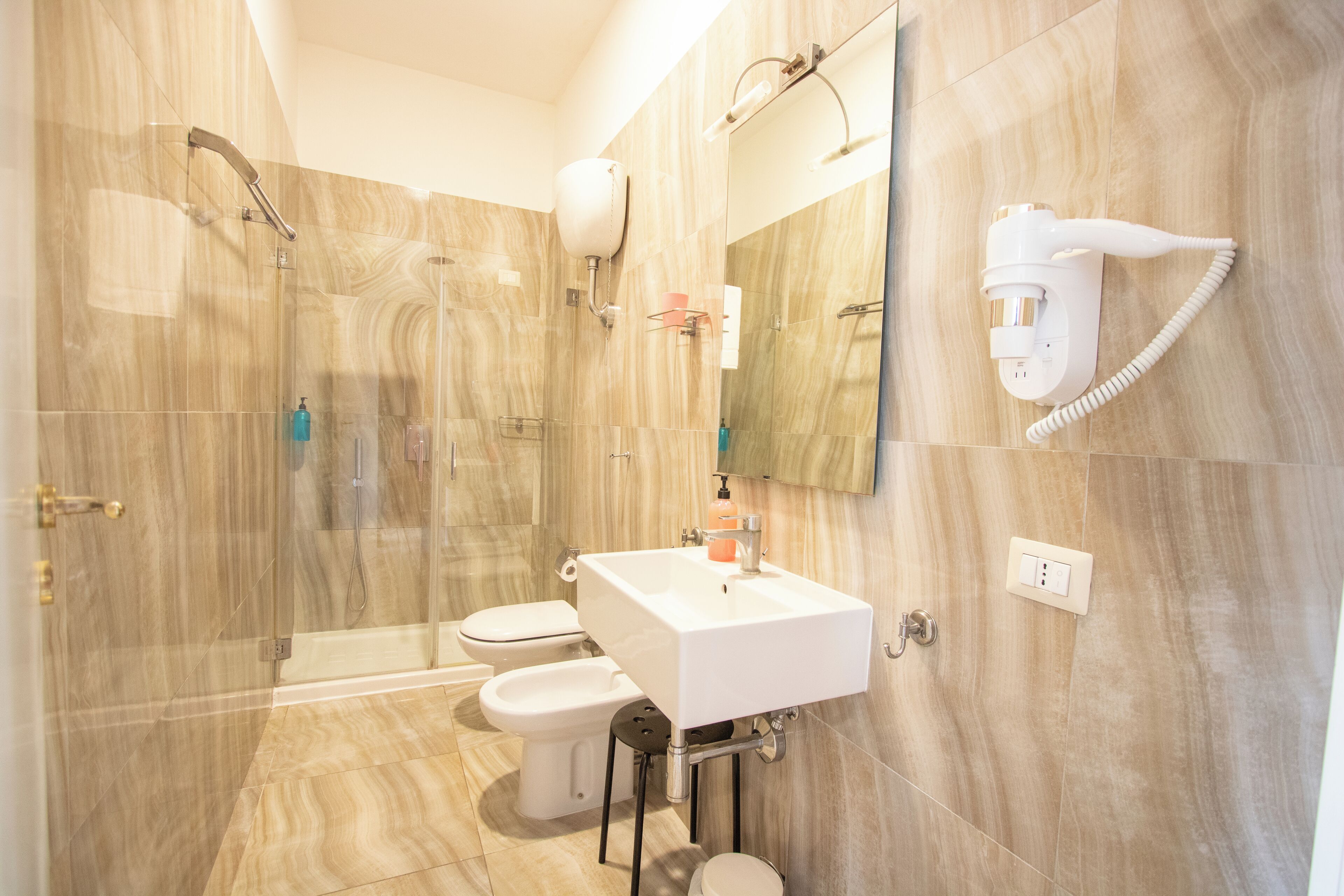 Un baño moderno con ducha, inodoro, bidé y un secador de pelo fijado en la pared.