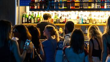 A bar area with various bottles and glasses, and people standing around.