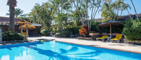 Una piscina con agua azul cristalina, rodeada de palmeras y un muro de piedra.