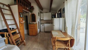 A kitchen with a wooden table and chairs, a refrigerator, cabinets, and a window with curtains.