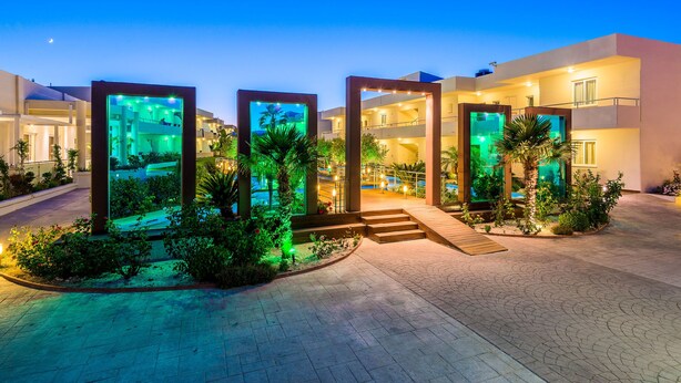 A modern hotel with a central courtyard, illuminated water features, and a well-lit entrance. - AFANDOU BAY SUITES HOTEL (Rhodes)