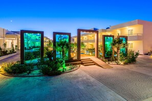 A modern hotel with a central courtyard, illuminated water features, and a well-lit entrance. - AFANDOU BAY SUITES HOTEL (Rhodes)