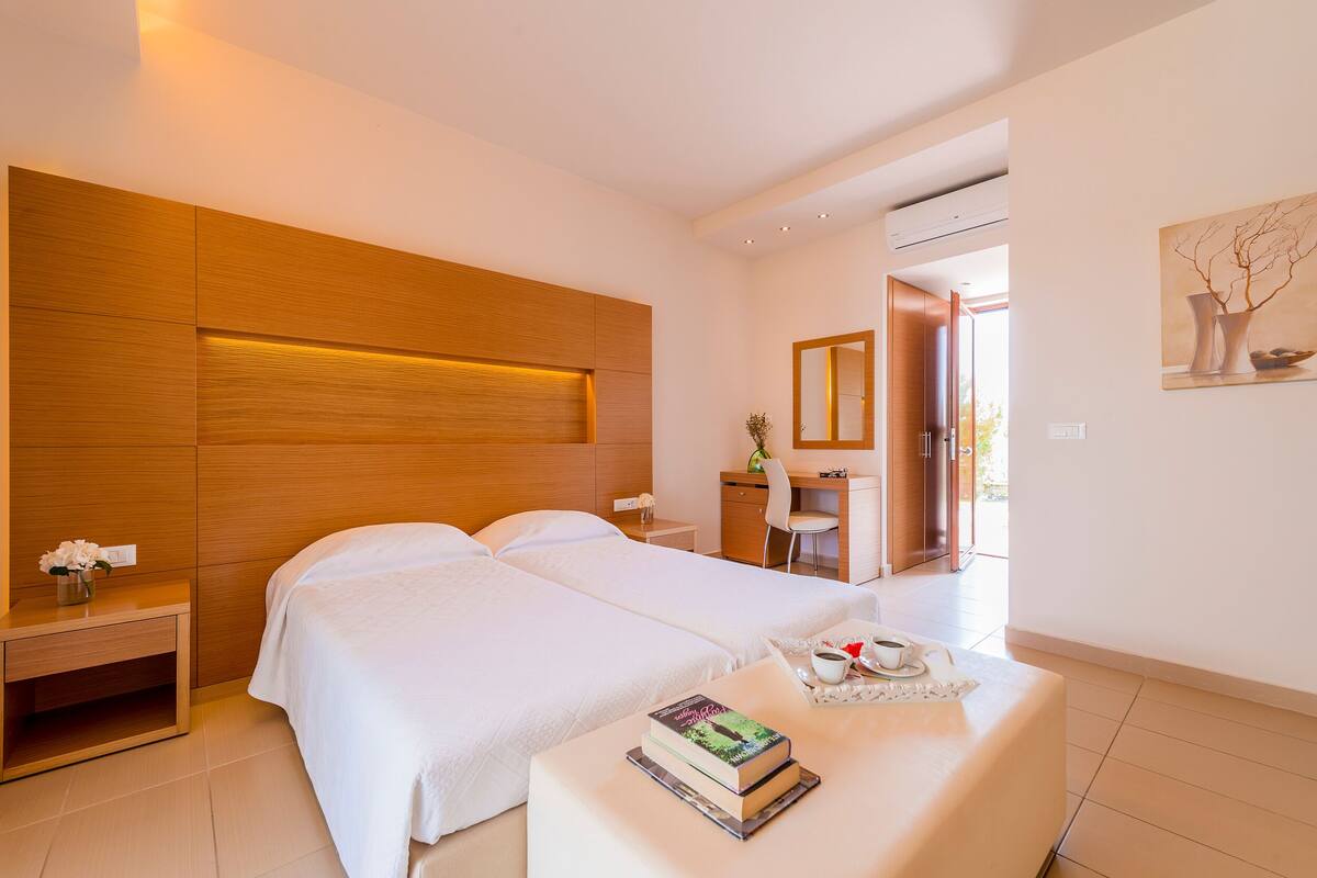 A modern hotel room with two beds, a desk, and a small seating area.