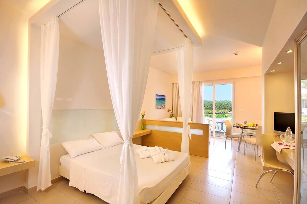 A hotel room with a bed, a desk, a chair, a balcony with a table and chairs, and a TV.