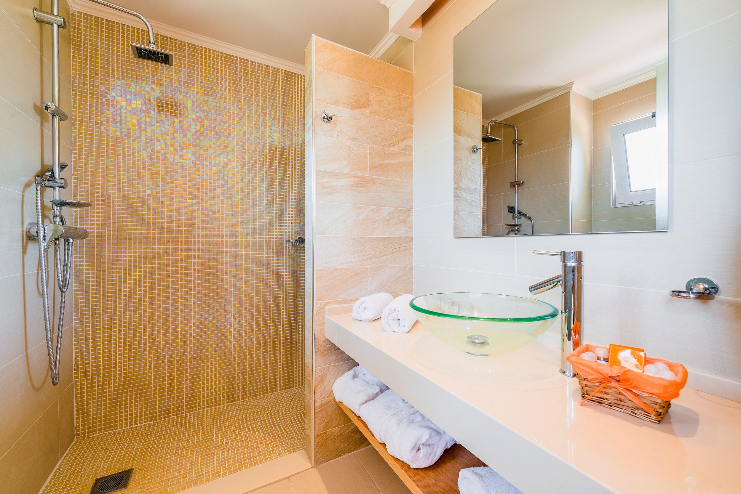 A modern bathroom with a glass sink, a shower with a tiled wall, and a mirror above the sink.