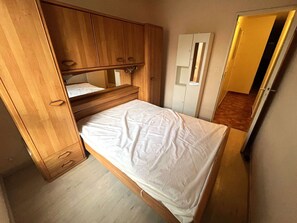 A compact room with a bed, wooden wardrobe, and a mirror. - Spacious T3 in Port Center, Residence with Pool, Cap d'Agde (Cap d'Agde)