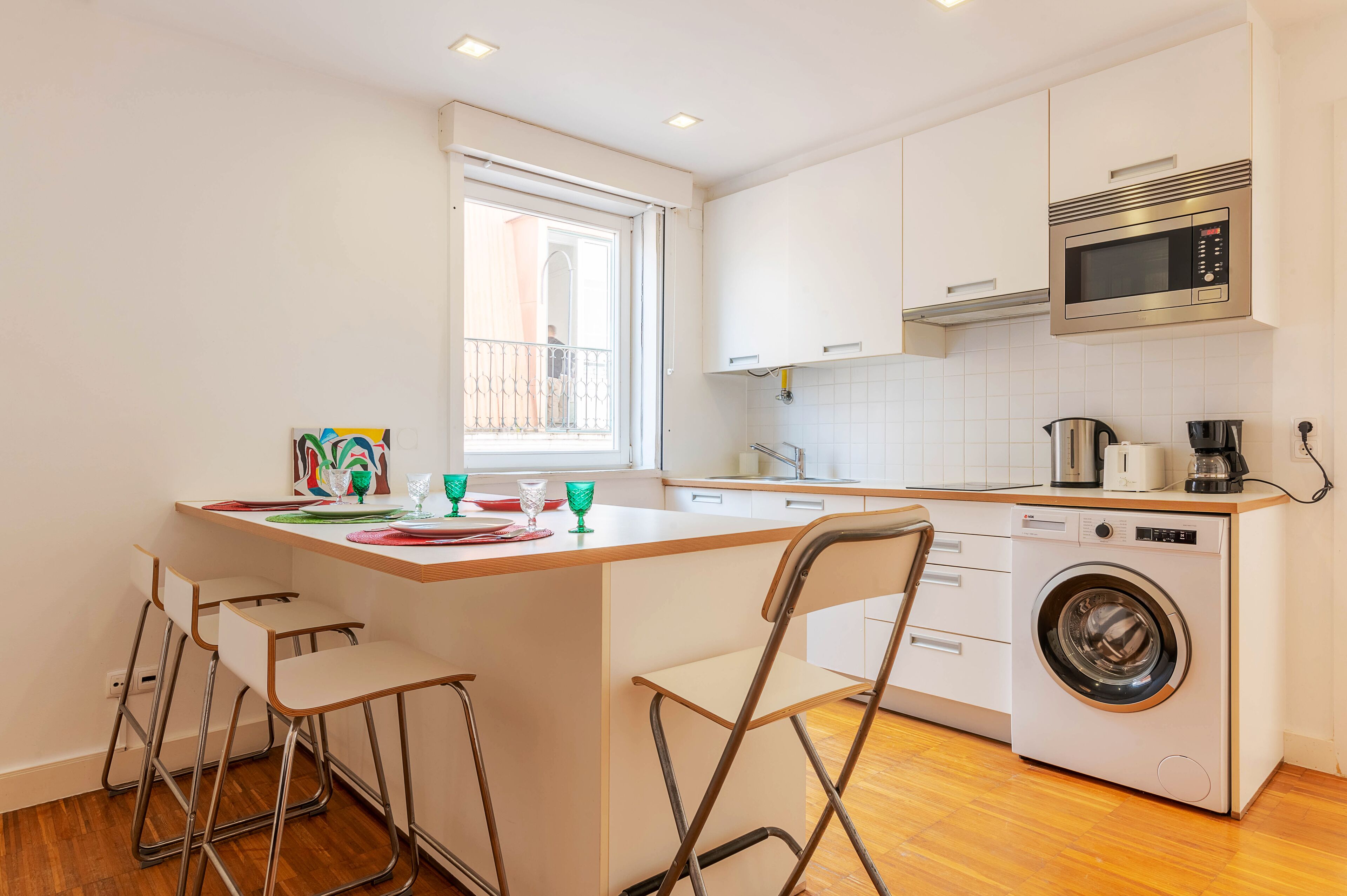 A compact kitchen with a washing machine, a microwave, and a window.