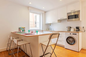 A compact kitchen with a washing machine, a microwave, and a window. - Portas do Bairro Alto (Lisbon)