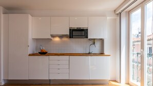 Ett modernt kök med vita skåp, en bänkskiva i trä, en inbyggd ugn och ett fönster med utsikt över byggnader.