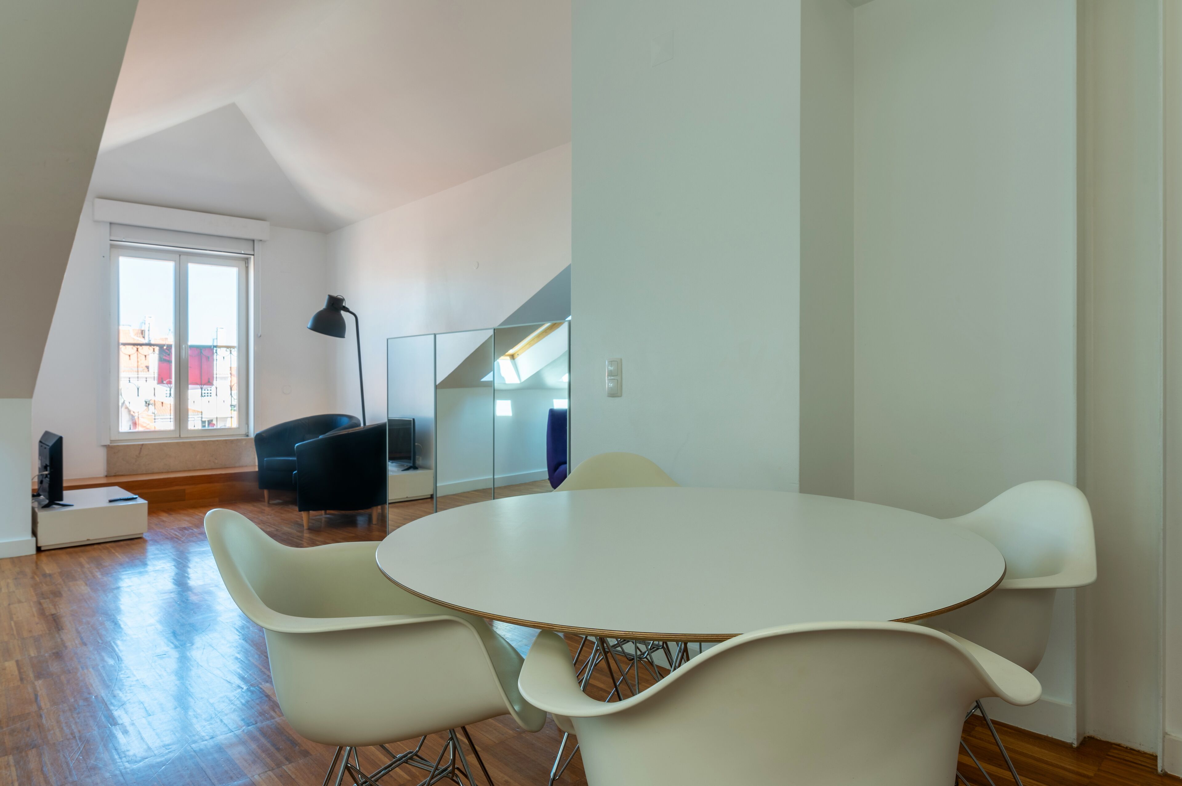 Un área moderna y abierta para sala y comedor, con un ventanal grande, una mesa redonda y muebles contemporáneos.