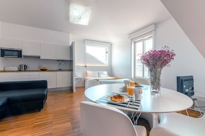 A modern kitchen with white cabinets, a black microwave, and a dining area with a round table, chairs, and a vase of flowers. - Portas do Bairro Alto (Lisbon)