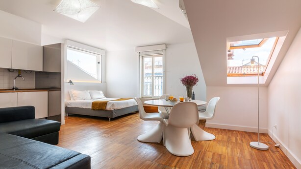 Ett modernt rum i loftstil med en matplats, en soffa, en säng och ett takfönster.