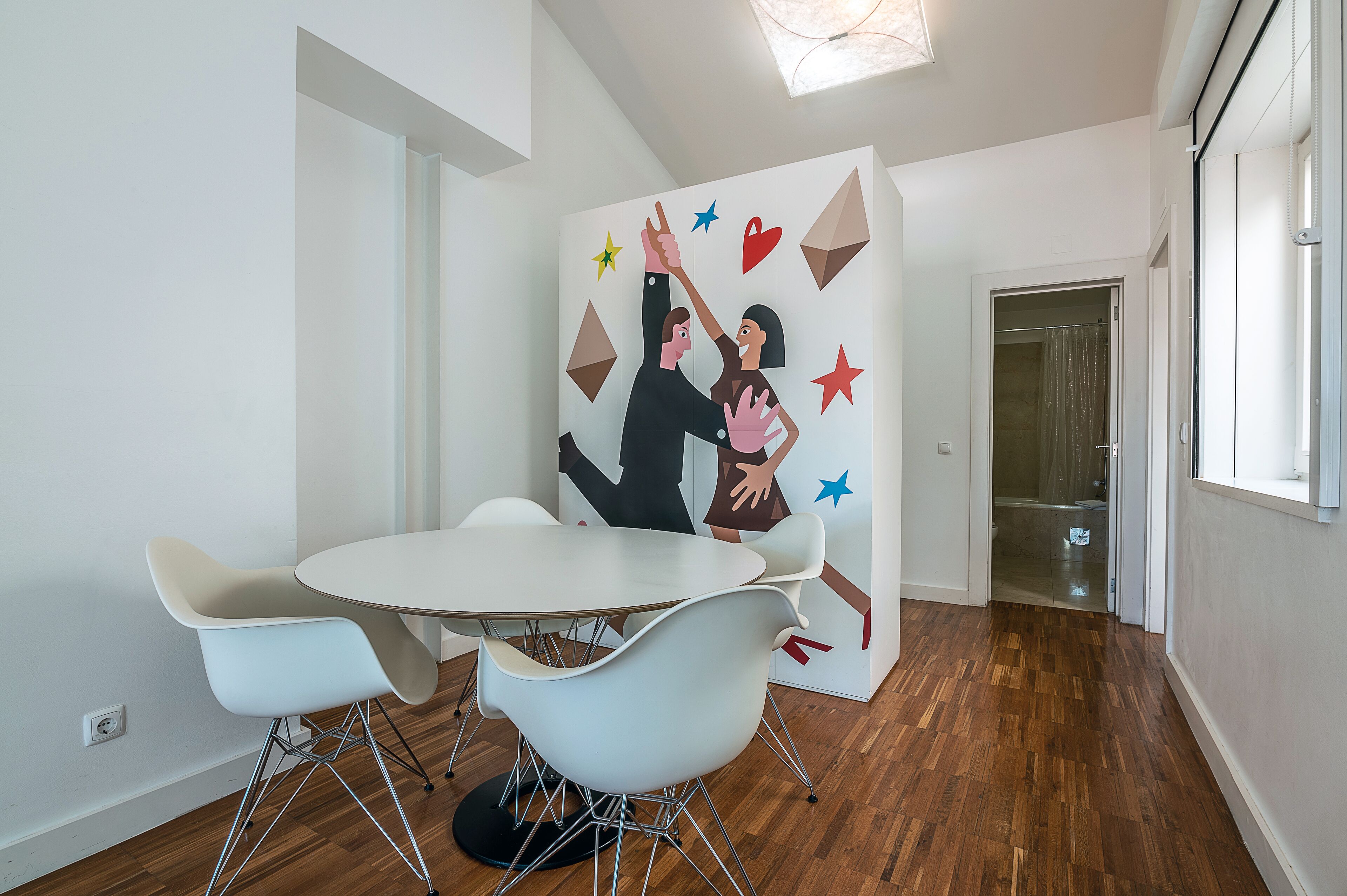 Una habitación moderna con una mesa redonda, dos sillas blancas y un mural en la pared.
