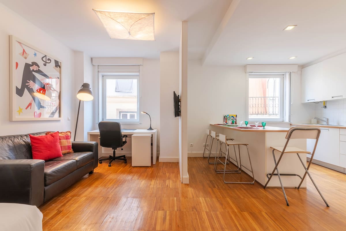 A modern apartment with a living area, a desk, and a kitchen.