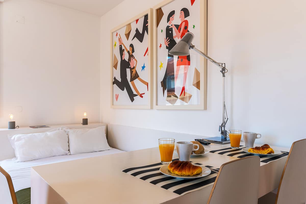 A hotel room with a bed, a dining table with breakfast, and two wall art pieces.