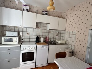 Una cocina compacta con armarios blancos, un microondas, un horno, un lavamanos y una pequeña mesa.