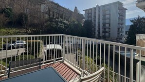 A balcony with a view of a multi-story building, a parking area, and a hillside with trees. - 35m² Apartment with South-East Terrace and Private Parking (Aix-les-Bains)