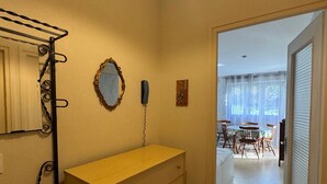 A room with a wooden dresser, a mirror, a telephone, and a door leading to a dining area with a table and chairs. - 35m² Apartment with South-East Terrace and Private Parking (Aix-les-Bains)